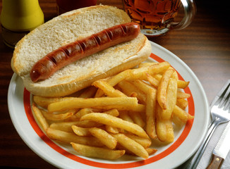 Un bocadillo con una barrita de pan y una sachicha frankfurt y un plato de patatas fritas.