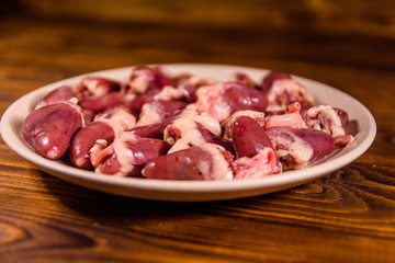 Ceramic plate with raw chicken hearts on wooden table
