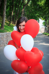 Girl in park with balloons smiling. Red and white colors.