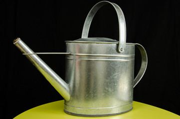 Old metallic watering can isolated in front of black background in studio.