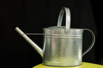 Old metallic watering can isolated in front of black background in studio.