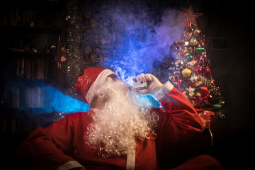 Obraz premium Santa Clause vaping electronic cigarette dressed as traditional Santa on a dark toned background with vape clouds. Selective focus.