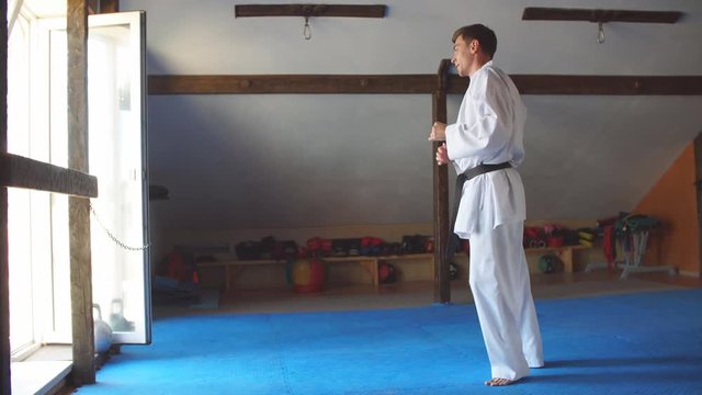 Caucasian Man in white kimono with black belt training karate in gym