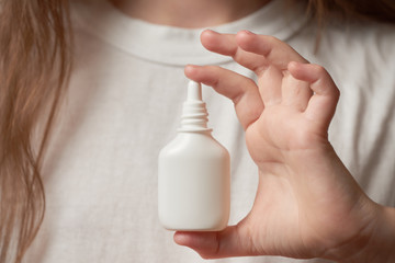 Girl in white tshirt holds in her hand bottle with allergy nasal drops.