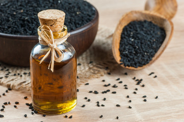 Black cumin seeds and essential oil with bowl and wooden shovel or spoon. Nigella Sativa in glass bottle. Organic herbal medicine for many diseases
