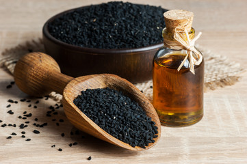 Black cumin seeds and essential oil with bowl and wooden shovel or spoon. Nigella Sativa in glass bottle. Organic herbal medicine for many diseases
