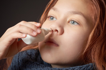 Sick girl with warm scarf on neck drips spray from nasal congestion.