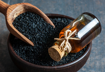 Black cumin seeds in bowl with wooden spoon essential oil , Nigella Sativa in glass bottle. Organic...