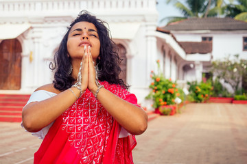 Young Indian woman in traditional sari red dress praying in a hindu temple goa india Hinduism.girl...