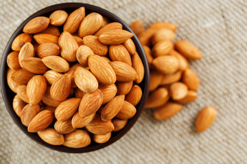 Almonds in a wooden cup on a burlap cloth background.