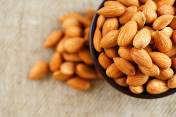 Almonds in a wooden cup on a burlap cloth background.