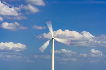 A rotating wind turbine and blue sky with clouds. Large three-bladed horizontal-axis wind turbines produce the overwhelming majority of windpower in the world today.