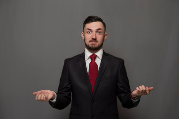 Successful young positive businessman holding out his hands saying welcome on gray background