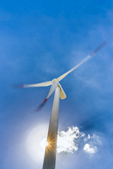 A rotating wind turbine and blue sky with clouds. Large three-bladed horizontal-axis wind turbines produce the overwhelming majority of windpower in the world today.
