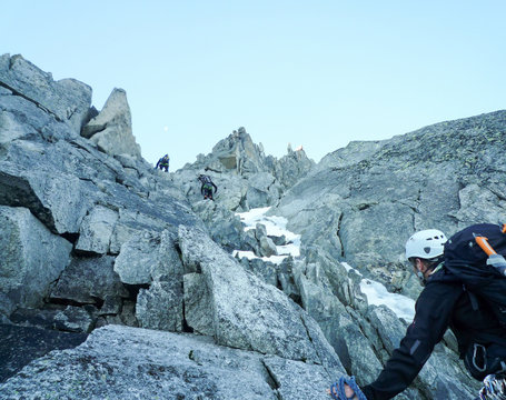 mountain guide looking up on a rocky climb in the French Alps with rope teams ahead of him