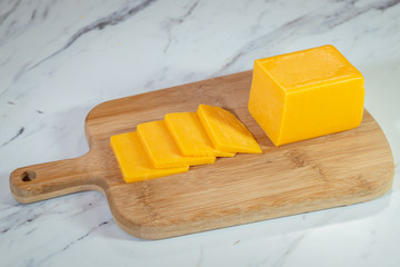 Block of cheese and cut slices on a wooden cutting board