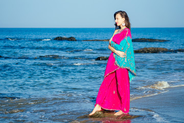 Young women wearing a pink blue saree on the beach goa India.girl in traditional indian sari on the shore of a paradise island among the rocks and sand enjoying the freedom and the morning