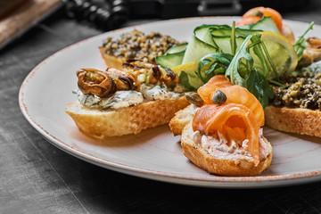 Tasty various italian sandwiches with seafood against rustic wooden background. Crostini with cheese, red fish, lemon and sliced olives, horizontal view with selective focus