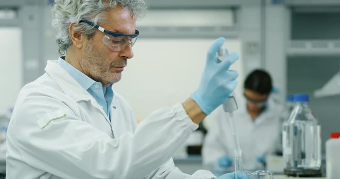 Portrait of male scientist with a pipette analyzes a liquid to extract the DNA and molecules in the test tubes in laboratory. Shot in 8K. Concept: research,biochemistry, pharmaceutical medicine