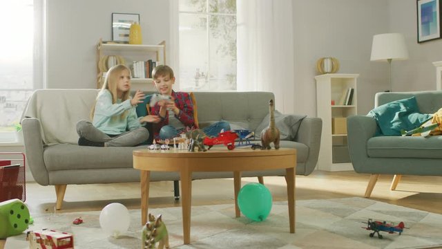 At Home: Smart Boy Playing in Video Game Console, Using Joystick Controller, His Older Sister Sits Near on Sofa and Cheers for Him. They Win and Celebrate Happily. Happy Children Playing Videogames.