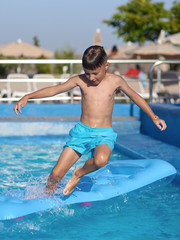 Boy having fun in swimming pool at hotel. He making jump from inflatable mattress into water.