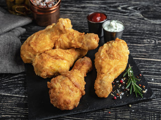 fried chicken leg in batter, red and white sauce on a dark surface