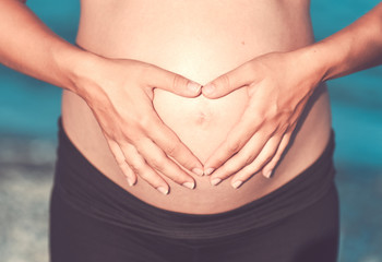 Fototapeta na wymiar Pregnant woman beach - hands in heart shape on belly