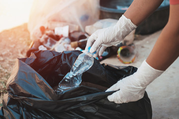 hand putting empty plastic bottle in to garbage black bag