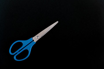 A pair of blue scissors on the left of a black background