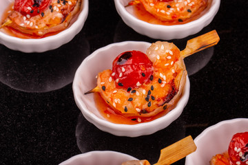 A tomato and a shrimp on a grill with sesame under hot sauce