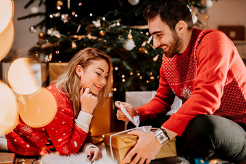 Happy couple enjoying Christmas morning and opening gifts wearing matching sweaters