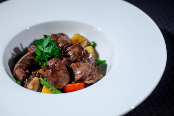 chicken liver in a white plate with vegetables and herbs on a dark background