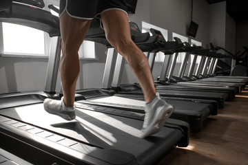Fototapeta na wymiar Young man running at treadmill in gym. Close-up