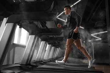 Young man running in sportwear with hoodie at treadmill in gym