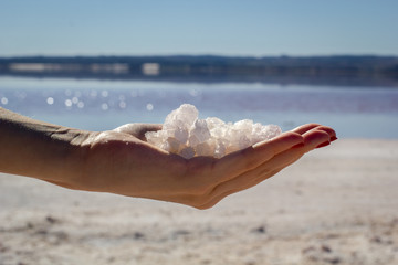 Female hand holding natural salt crystals on the background of a salt lake, side view close up