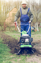Man working in the spring garden with tiller machine
