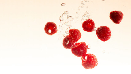 raspberry fruits making splash in water orange pastel background