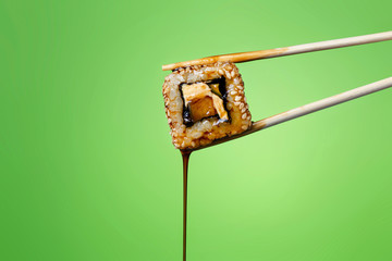succulent roll between chopsticks on a colored background, drops of soy sauce dripping from sushi,...