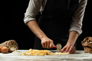 The chef cuts Italian pasta dough. Against a dark background. A concept for preparing delicious food, Italian cuisine and recipes. Culinary recipes