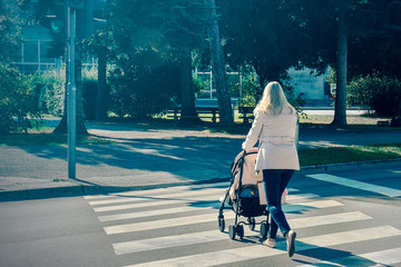 mom crosses the pedestrian crossing. She's pushing stroller with her baby across the street