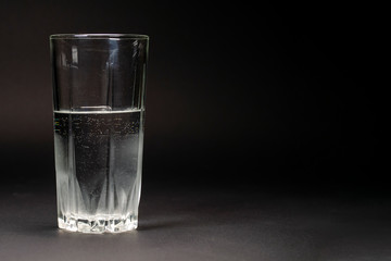 Transparent glass of cold water with small bubbles on the walls on a dark background