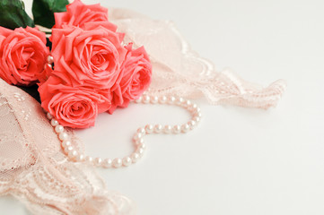 Obraz na płótnie Canvas Delicate feminine theme. Pink coral roses trend color on a pale pink bra and pearl necklace on a white background. top view. close up. Stylish lingerie flat lay. selective focus