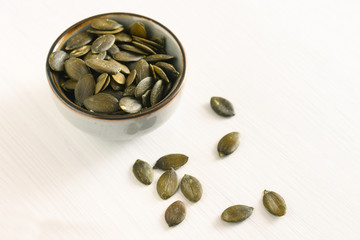 pumpkin seeds in a small bowl on a white table, healthy snack and diet concept, copy space
