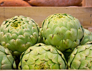 Obraz premium wooden box full of artichokes in French food market with sweet potatoes background