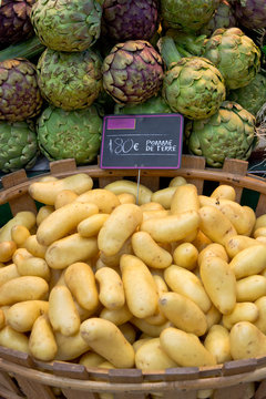Basket full of potatoes with artichokes in the background at French food market
