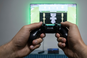 Man playing video game. Hands holding console controller. Football or soccer game on the television. Widescreen tv hangs on the wall