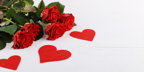 Red roses and hearts on a white wooden table. Concept of Women's Day or St. Valentine. Copy space.