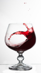 red wine splashing out of a glass, on white bacground