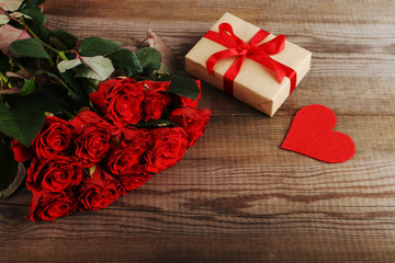 A bouquet of red roses, a gift and hearts on wooden table. Concept of Women's Day or St. Valentine. Copy space.