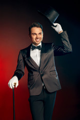 Professional Occupation. Showman in suit standing isolated on wall with cane holding hat up...